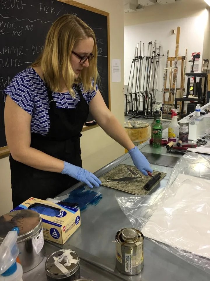 Kathryn wearing blue gloves inking a woodblock.