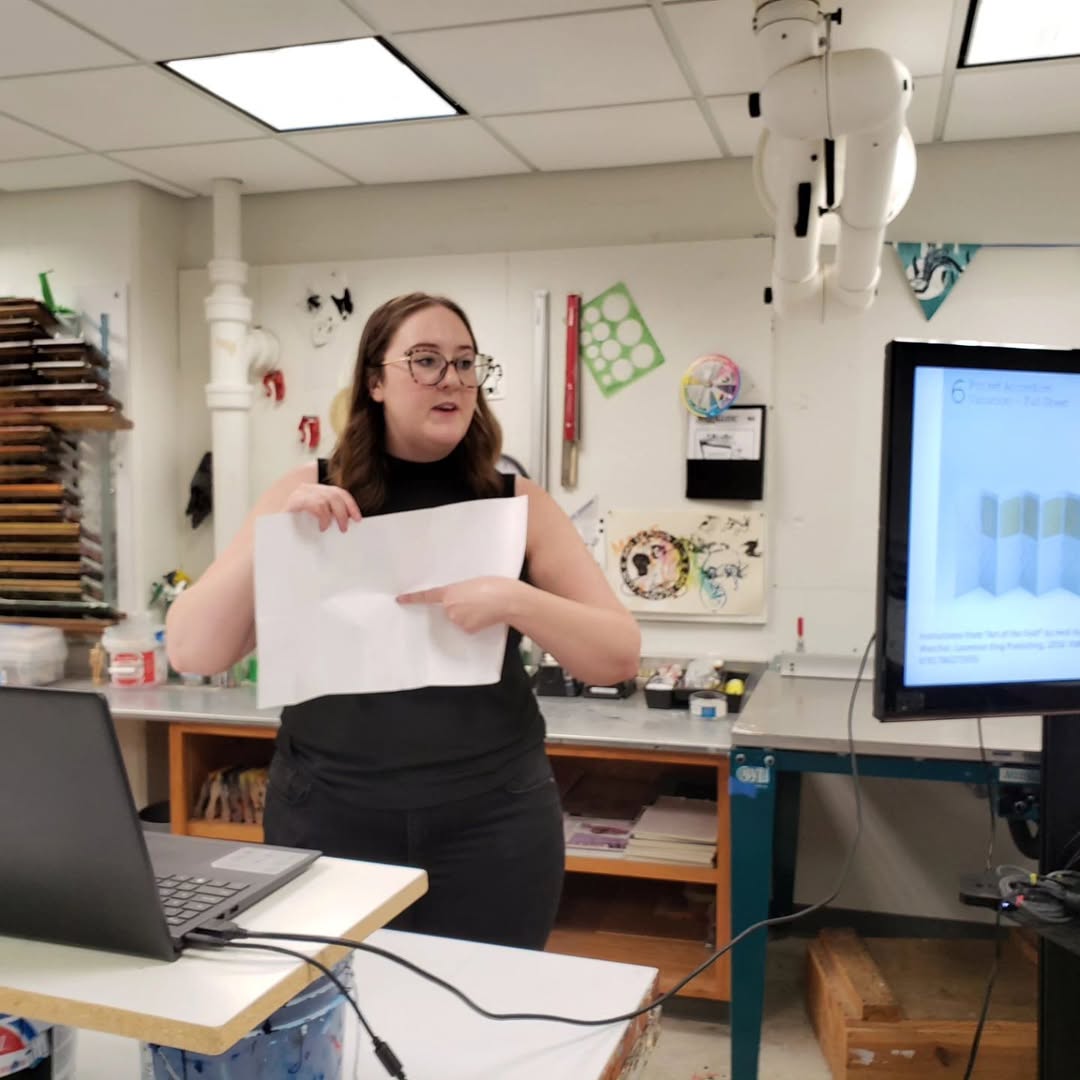 Kathryn holding up a piece of paper and pointing to it in a printmaking studio